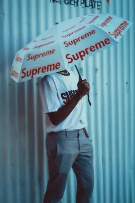 a man standing in front of a wall holding an umbrella, inspired by Bert Stern, unsplash, supreme, playboi carti, * * * * *, sup