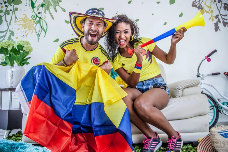 a couple of people sitting on top of a couch, inspired by Victor Meirelles, pexels contest winner, antipodeans, carnaval de barranquilla, flags, sports clothing, at the world cup