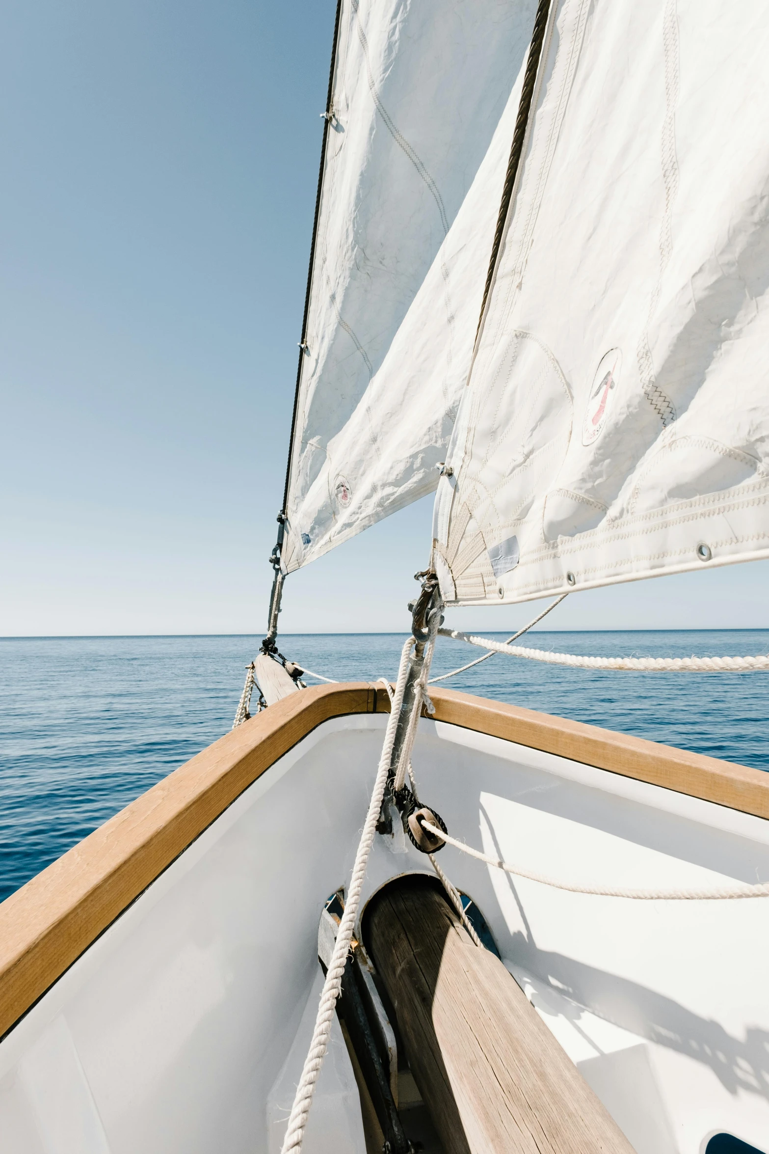 a view of the ocean from the bow of a sailboat, inspired by Willem van de Velde the Elder, unsplash, minimalism, clear blue skies, white cloth in wind shining, wooden boat, snacks