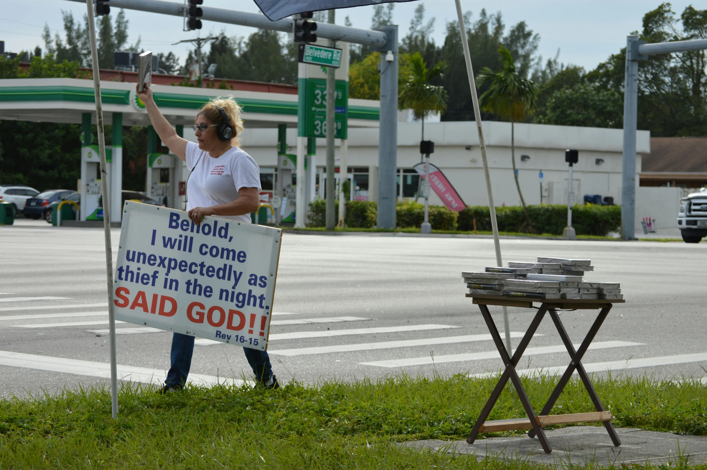 a man holding a sign in front of a gas station, flickr, blessing palms, standing bravely on the road, basil gogos, photograph credit: ap