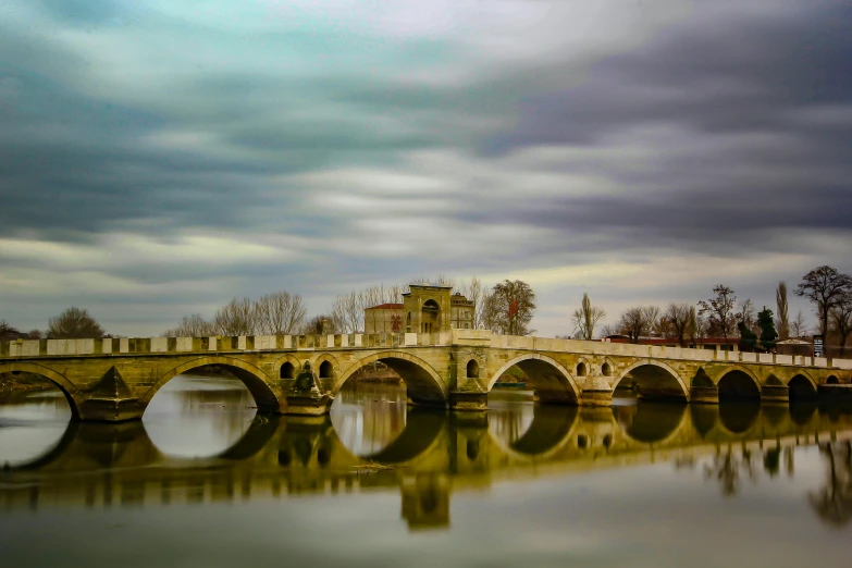 a bridge over a body of water under a cloudy sky, a picture, pexels contest winner, neoclassicism, estefania villegas burgos, old bridge, coloured photo, many reflections