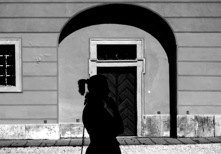 a black and white photo of a person walking in front of a building, a black and white photo, woman silhouette, taking a picture, arched doorway, biedermeier