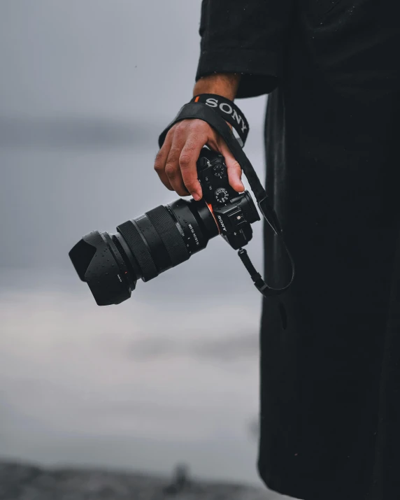 a person holding a camera near a body of water, sony a7, macro lens product photo