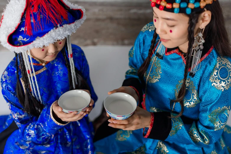 a couple of young girls sitting next to each other, inspired by Hu Zao, trending on unsplash, cloisonnism, offering a plate of food, costume with blue accents, holding a bottle of arak, mongolia