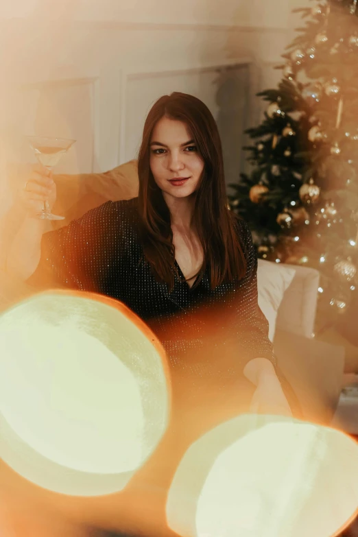 a woman sitting on a couch in front of a christmas tree, by Julia Pishtar, pexels contest winner, hanging out with orbs, wine, orange and black tones, handsome girl