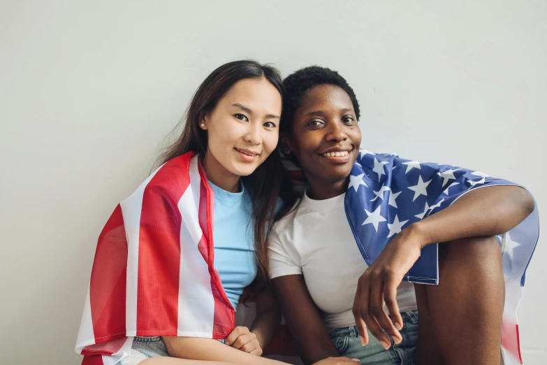 a couple of women sitting on top of a bed, pexels, american barbizon school, american flags, ethnic group, ad image, on a white table