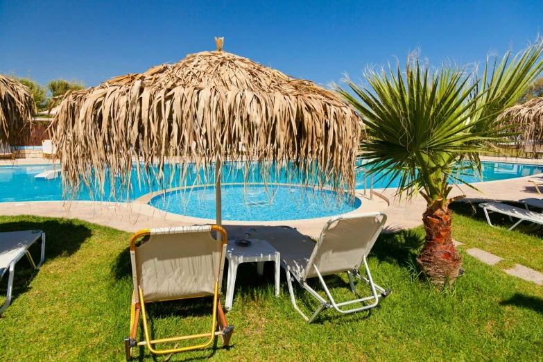 a group of lawn chairs sitting next to a swimming pool, by Matthias Stom, unsplash, varadero beach, with a lush grass lawn, moroccan, parasol