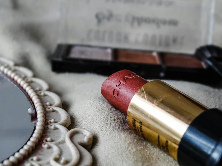 a red lipstick sitting on top of a table next to a mirror, inspired by Adélaïde Labille-Guiard, pexels contest winner, oil pastels and gold, chanel, coral brown hair, chalked