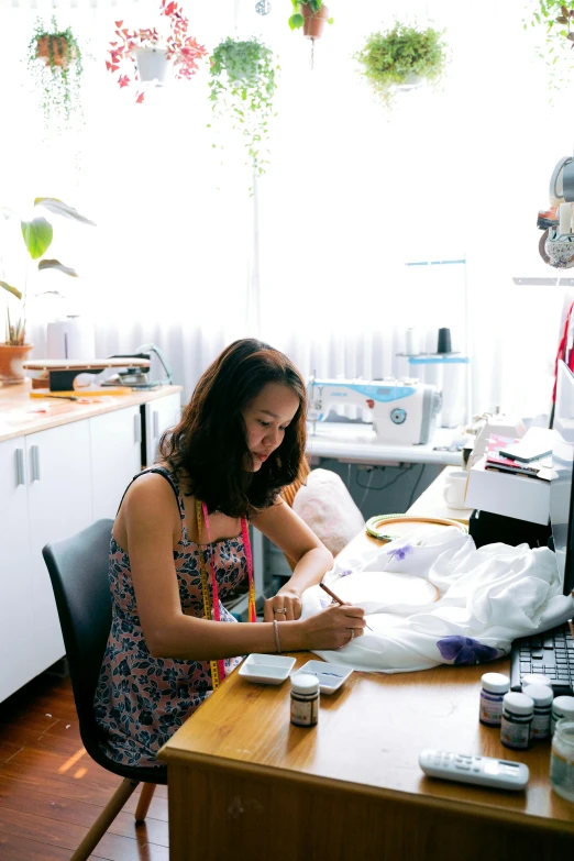 a woman sitting at a desk writing on a piece of paper, by Elizabeth Durack, process art, garments, digital medical equipment, wearing a designer top, crafts and souvenirs