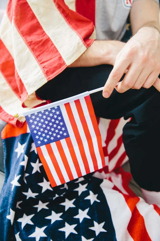 a person sitting on the ground holding an american flag, closeup of arms, 🚿🗝📝