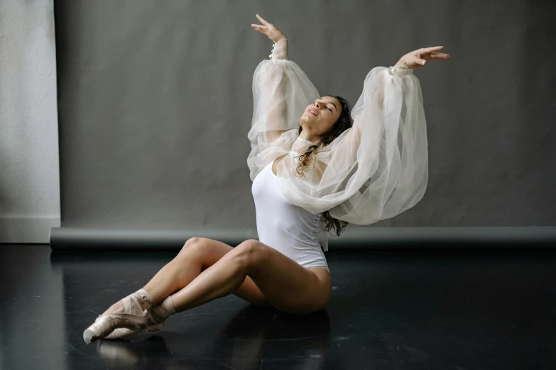 a woman sitting on the floor with her arms in the air, a portrait, by Elizabeth Polunin, pexels contest winner, arabesque, wearing white leotard, silver，ivory, covered in transparent cloth, satisfied pose