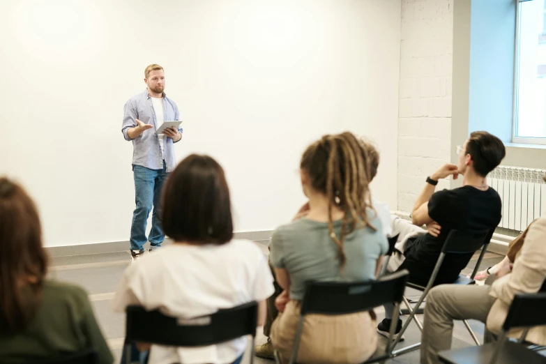 a man standing in front of a group of people, trending on unsplash, academic art, white wall coloured workshop, sitting, teaching, lachlan bailey