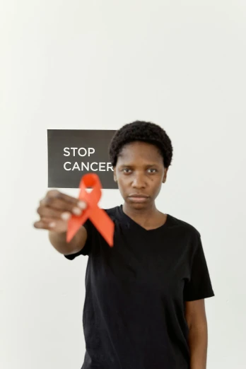 a woman holding a sign that says stop cancer, by Lily Delissa Joseph, pexels contest winner, red ribbon, maria borges, thin young male, 2 0 0 0 s
