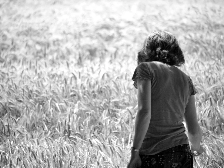 a woman standing in a field of tall grass, a black and white photo, pexels, girl walking in wheat field, grief, looking outside, compassion