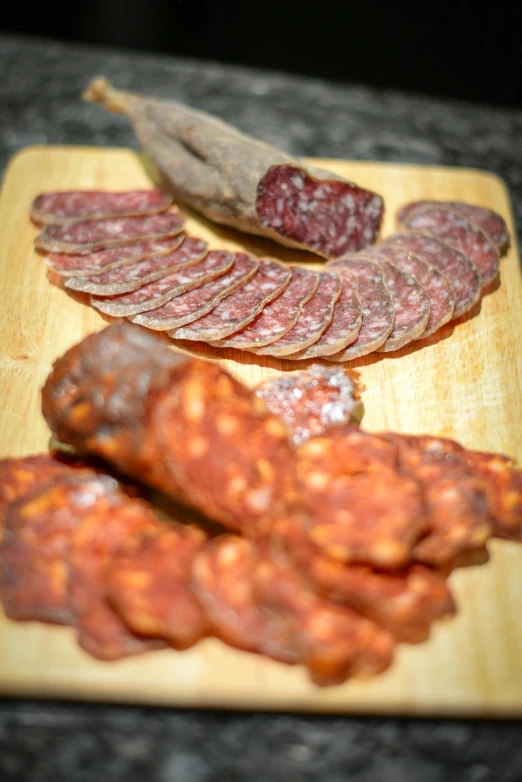 a wooden cutting board topped with slices of meat, chorizo sausage, photograph taken in 2 0 2 0, paisley, crimson themed