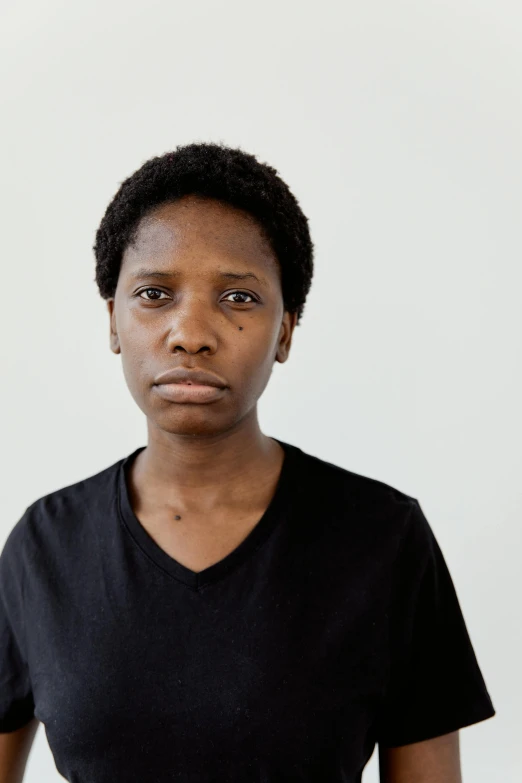 a woman standing in front of a white wall, by Lily Delissa Joseph, shaven face, without makeup, maria borges, concerned expression