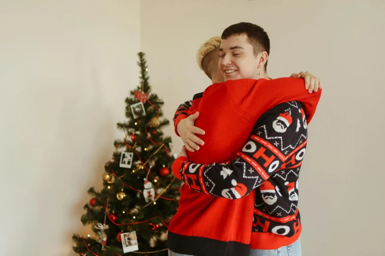 a man hugging a woman in front of a christmas tree, a photo, pexels, realism, background image, two men hugging, teenage boy, wearing festive clothing