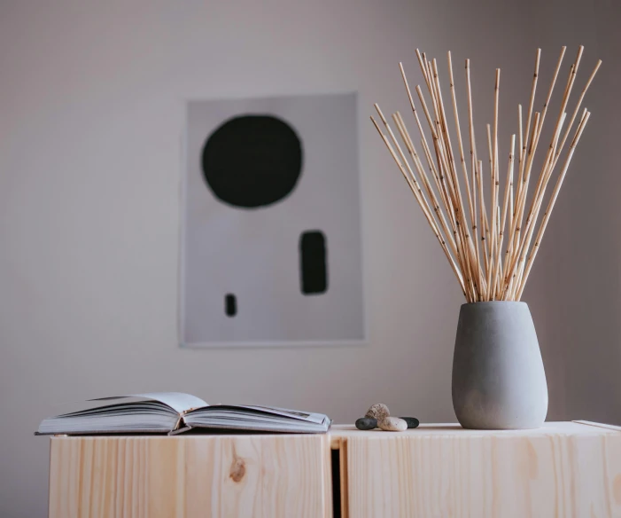 a vase sitting on top of a wooden table next to a book, a minimalist painting, trending on pexels, incense, reeds, displayed on an altar, product display photograph