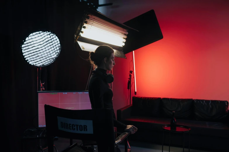 a woman sitting in a chair in front of a red light, behind the scenes, cinema studio lights, vollumetric lighting, production ig