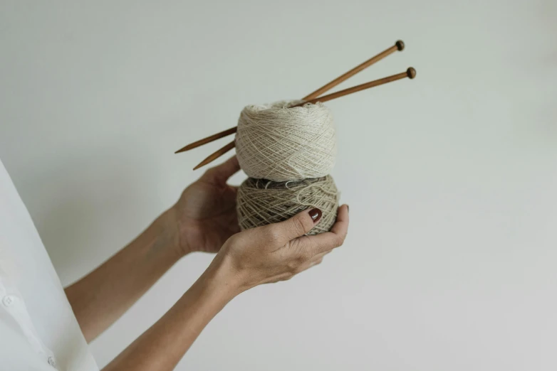 a woman holding a ball of yarn and knitting needles, inspired by Sarah Lucas, unsplash, arts and crafts movement, beige cream natural muted tones, unknown artist, made of bamboo, uncrop