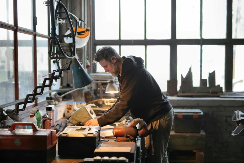 a man in a workshop working on a piece of wood, pexels contest winner, arbeitsrat für kunst, scrap metal on workbenches, sydney hanson, olafur eliasson, brass equipment and computers