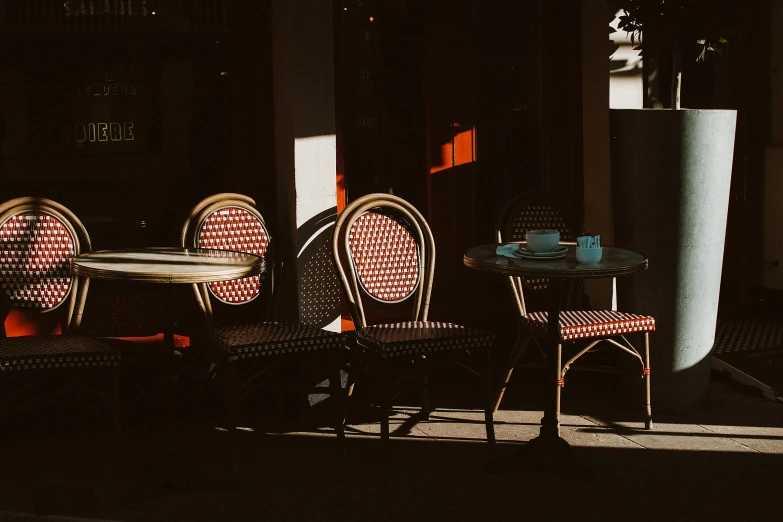 a couple of chairs and a table in a room, inspired by Brassaï, unsplash contest winner, in a sidewalk cafe, sparkling in the sunlight, red and brown color scheme, contre jour