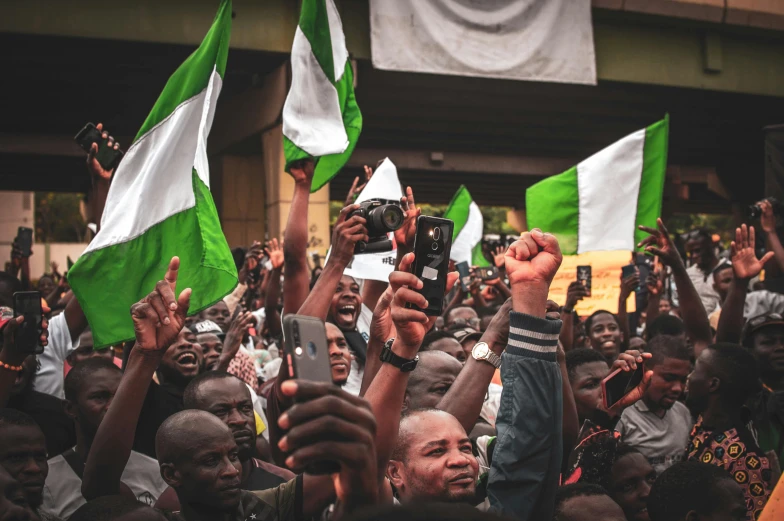 a crowd of people holding up green and white flags, a photo, by Matija Jama, pexels, happening, adebanji alade, hold up smartphone, 🚿🗝📝, crowd hails him