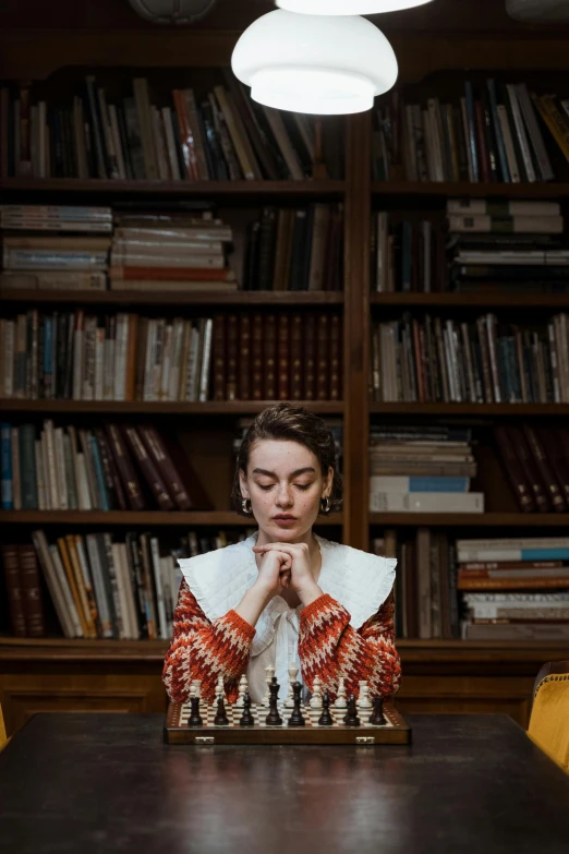 a woman sitting at a table with a chess board in front of her, inspired by Sofonisba Anguissola, unsplash contest winner, inside a library, dressed like a cleric, maxim sukharev, trending photo