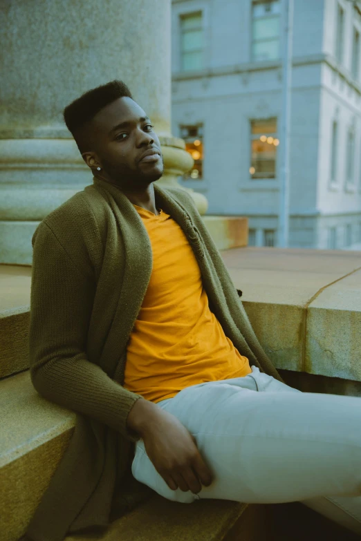 a man sitting on the steps of a building, an album cover, inspired by Theo Constanté, pexels contest winner, warm color clothes, jaylen brown, graceful gaze, yellow carpeted