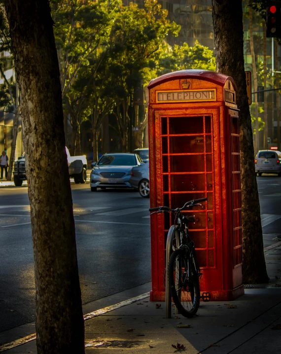 a red phone booth sitting on the side of a street, a photo, pexels contest winner, 🚿🗝📝, square, bicycle, nice afternoon lighting