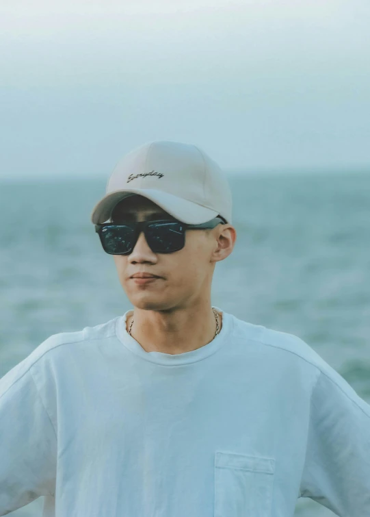 a man standing on top of a beach next to the ocean, by Jang Seung-eop, unsplash, realism, wearing sunglasses and a cap, discord profile picture, wearing casual clothing, headshot profile picture