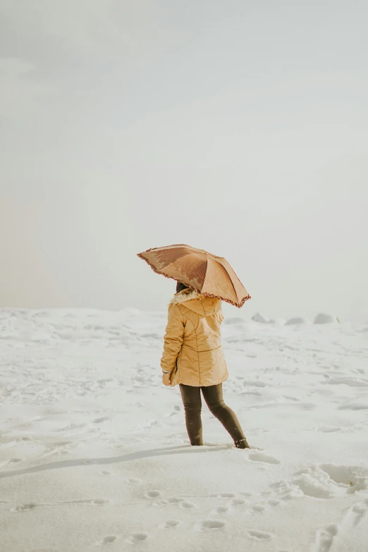 a person standing in the snow with an umbrella, inspired by Zhang Kechun, trending on unsplash, conceptual art, caramel. rugged, sunny day time, woman, beige