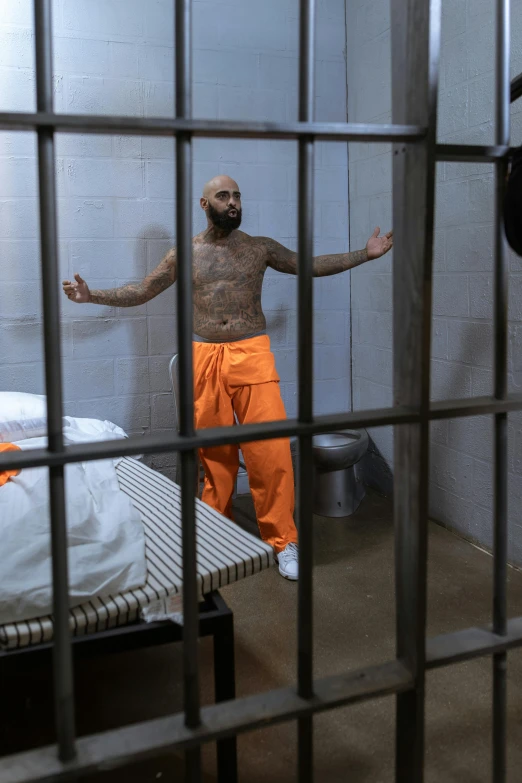 a man standing in a jail cell next to a bed, tattooed, riyahd cassiem, h3h3, lgbtq