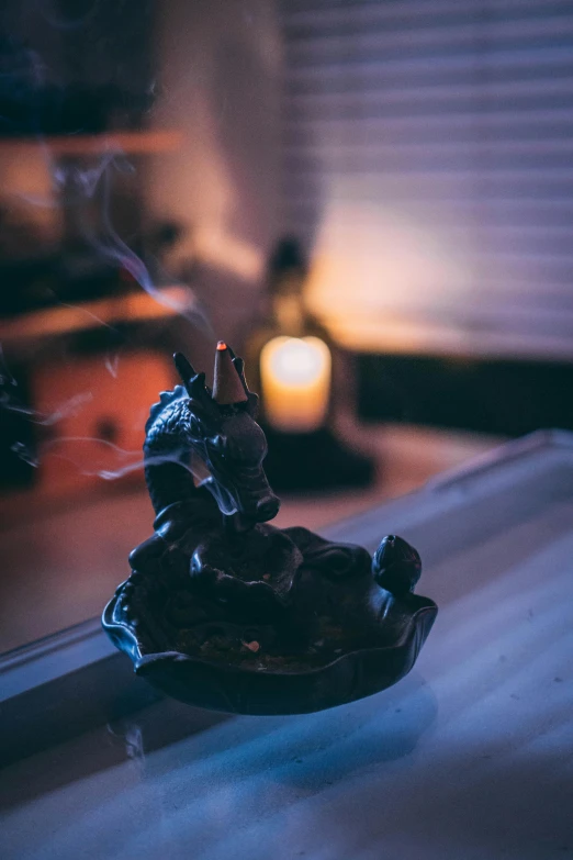 a statue sitting on top of a table next to a lit candle, incense, profile image, environmental shot, bath