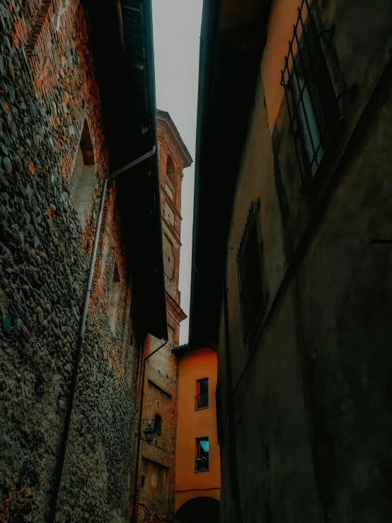 a couple of buildings that are next to each other, a picture, inspired by Eliseu Visconti, pexels contest winner, renaissance, in an alleyway during the purge, dark grey and orange colours, instagram story, towering over your view