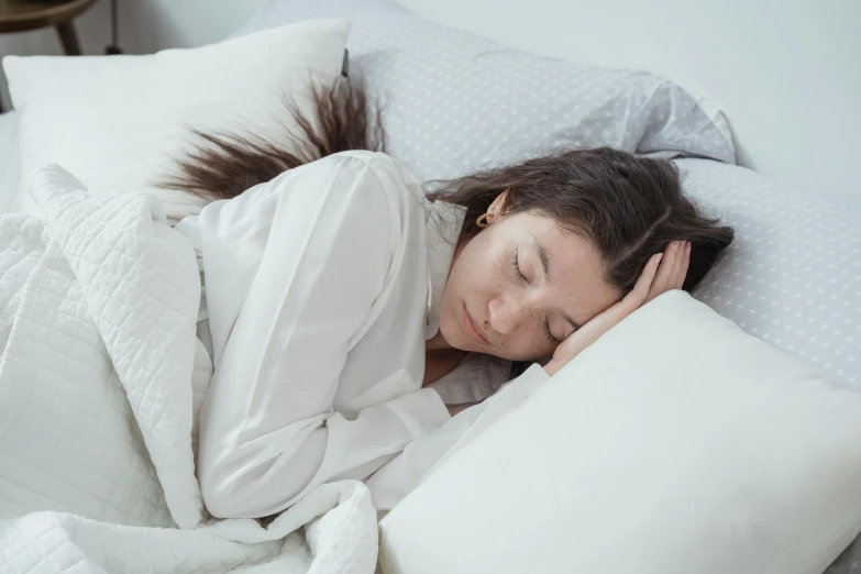 a woman laying in bed with her eyes closed, trending on pexels, on grey background, girl with brown hair, freezing, very comfy]