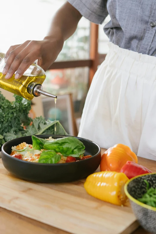 a woman pouring olive oil into a bowl of vegetables, pexels, renaissance, on kitchen table, college, black, colorful scene