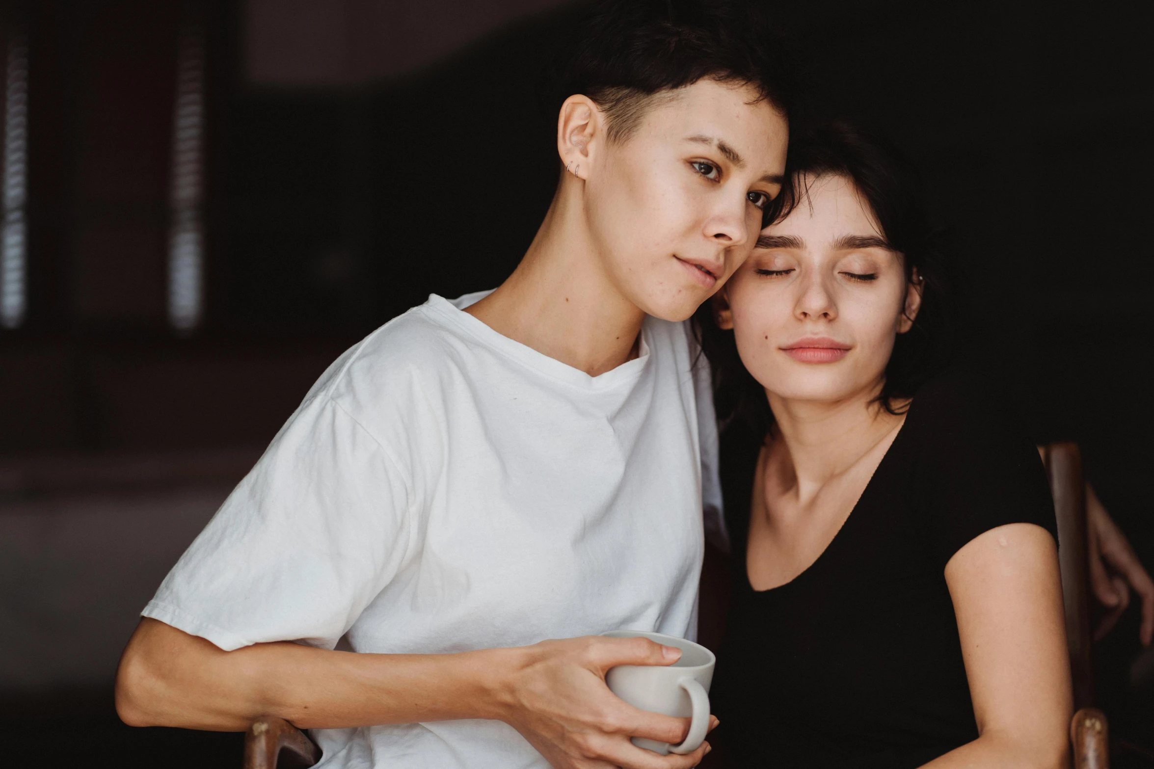 a man and a woman standing next to each other, trending on pexels, antipodeans, lesbian embrace, sitting on a mocha-colored table, woman with black hair, portait image