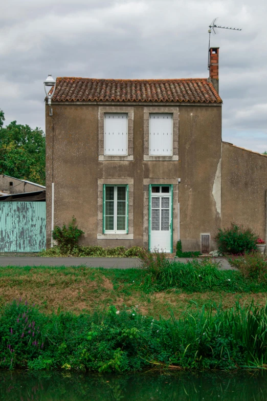 a house sitting next to a body of water, an album cover, inspired by Théodore Rousseau, pexels contest winner, french village exterior, boarded up, front view 1 9 9 0, color photograph