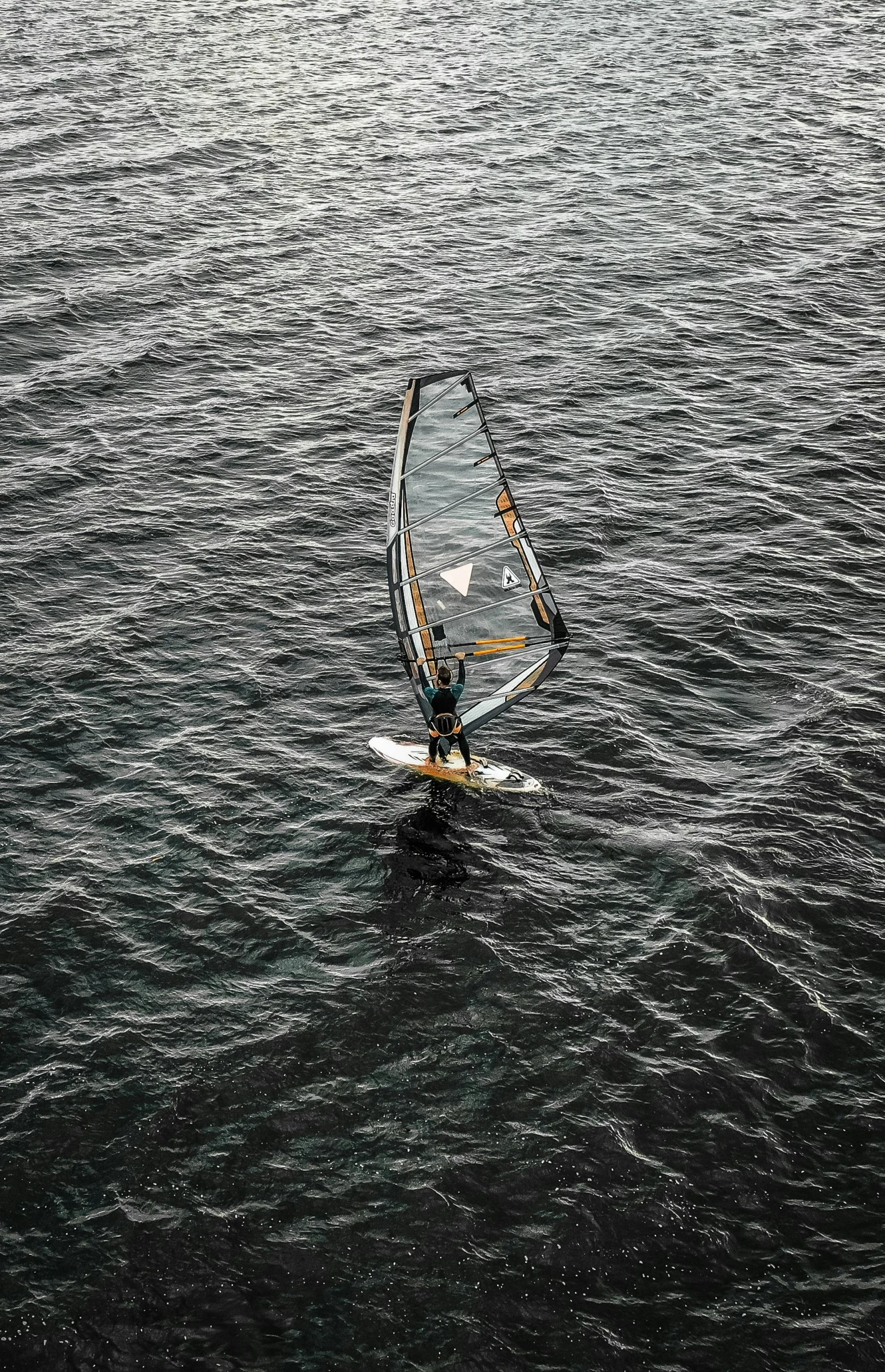 a person windsurfing in a body of water, looking down from above, body of water, in the water