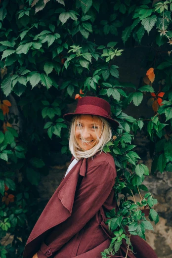a woman in a red coat and hat posing for a picture, a picture, inspired by Florence Engelbach, pexels contest winner, amongst foliage, the rad hatter, avatar with a blond hair, maroon red