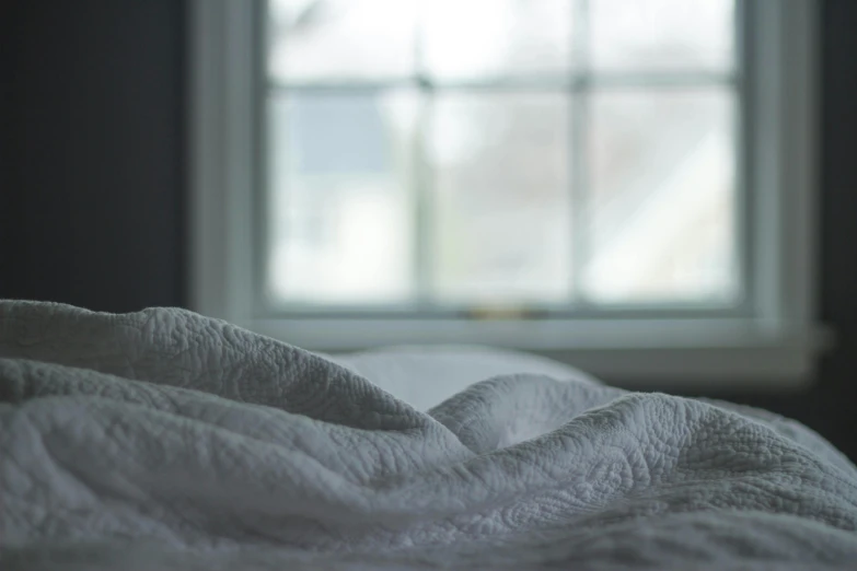 an unmade bed with a window in the background, unsplash, soft and fluffy, moonlight grey, shot from the side, angled shot