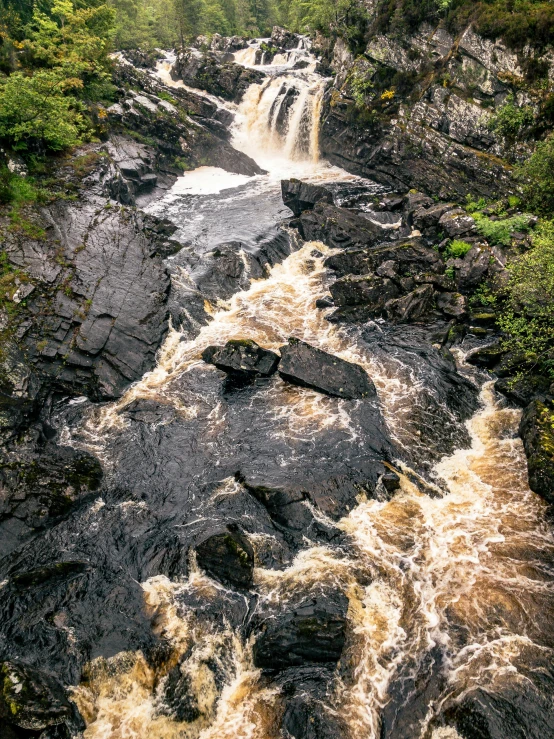 a river running through a lush green forest, by Terese Nielsen, pexels contest winner, hurufiyya, with lots of dark grey rocks, gold waterfalls, scottish highlands, high angle view