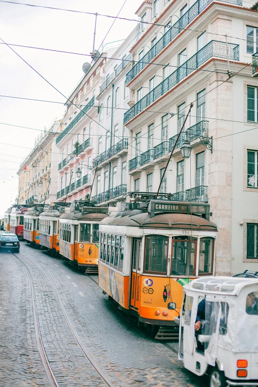 a couple of trolleys driving down a street next to a tall building, inspired by Almada Negreiros, trending on unsplash, white marble buildings, preserved historical, 🚿🗝📝