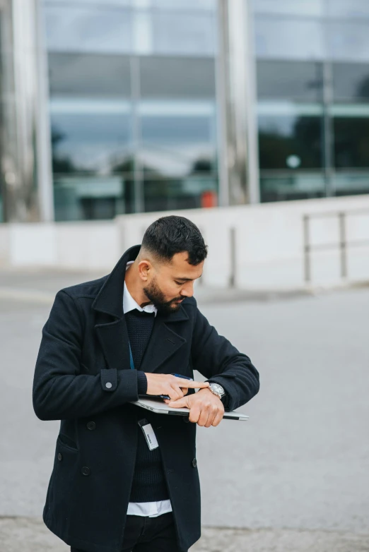 a man in a black coat looking at his cell phone, pexels contest winner, holding a clipboard, wearing a watch, khyzyl saleem, security agent