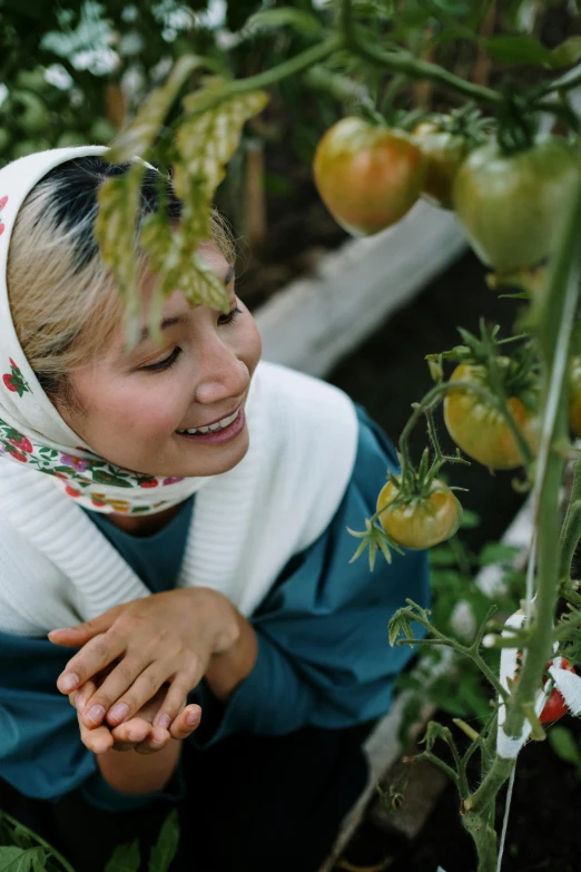 a woman standing next to a bunch of tomatoes, inspired by Li Di, unsplash, wearing a head scarf, mutahar laughing, next to a plant, film still