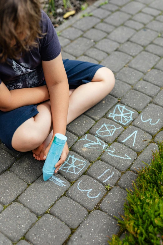 a little girl sitting on the ground writing on the sidewalk, chalk art, by Adam Marczyński, pexels contest winner, teal-neon viking runes, geometric figures, thumbnail, outdoor photo