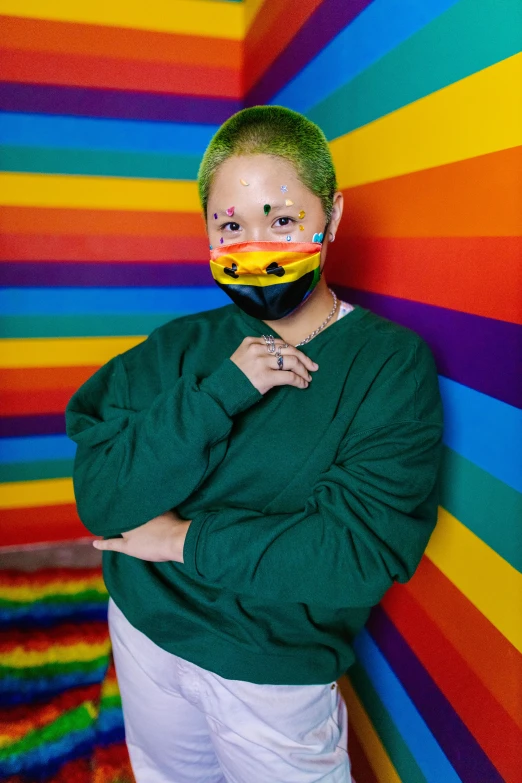 a man standing in front of a colorful wall, an album cover, inspired by Okuda Gensō, trending on pexels, short green hair, the mask covers her entire face, teddy fresh, lesbians