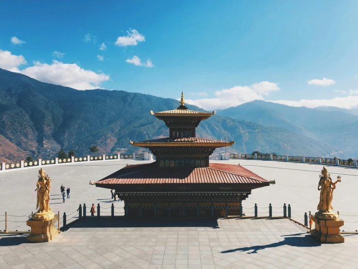 a group of statues in front of a building with mountains in the background, by Julia Pishtar, pexels contest winner, cloisonnism, bhutan, square, view from above, golden pillars