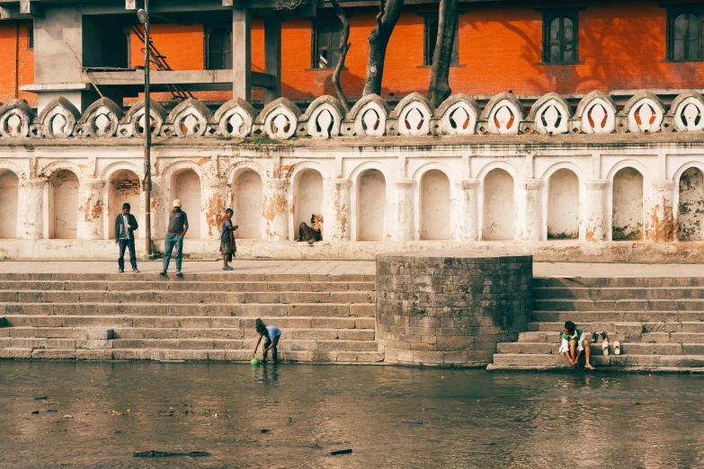 a group of people standing next to a body of water, pexels contest winner, hurufiyya, nepali architecture buildings, stepping stones, thumbnail, gray and orange colours